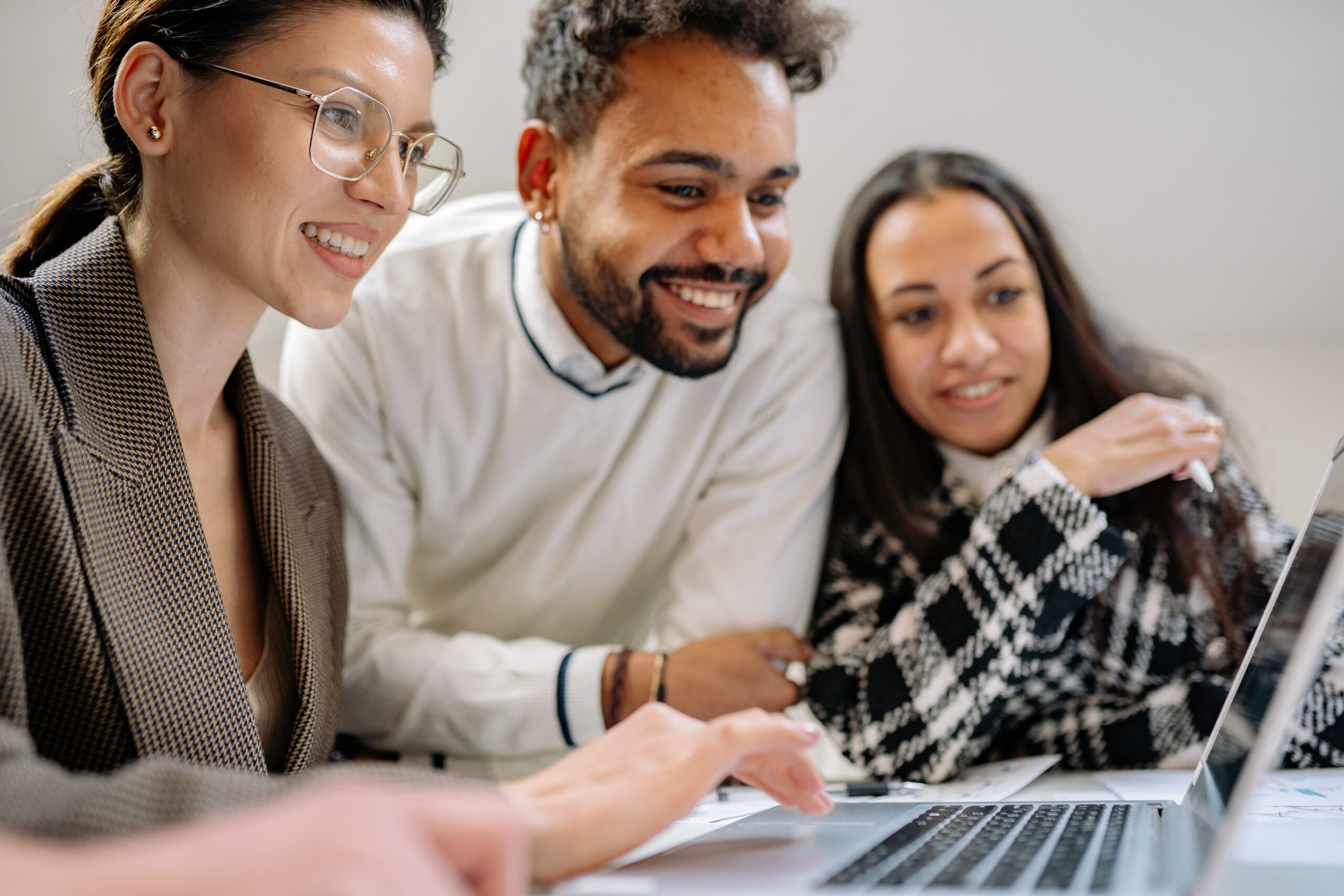 Three people smiling while working on a shared laptop.